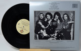 A vinyl record partially pulled from its outer paper sleeve, showing the black record on the left and the back cover with printed tracklist and a black-and-white band photo on the right.