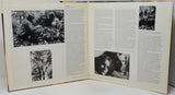 An open vintage book or magazine spread, showing two cream-colored pages filled with dense black text and several black-and-white photographs, photographed against a light neutral background.