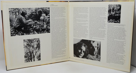 An open vintage book or magazine spread, showing two cream-colored pages filled with dense black text and several black-and-white photographs, photographed against a light neutral background.