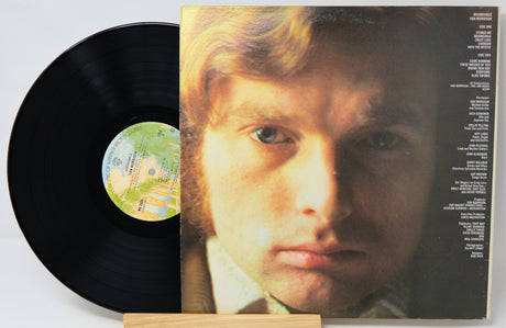 A vinyl record partially pulled from its album cover, showing a close-up portrait of a man on the cover and a black record disc with a colorful center label.