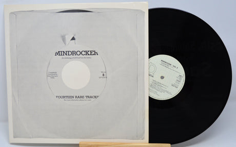 A vinyl record and its cover with the label 'Mindrocker Volume 8' and a white and black design. The record is flipped, showing the other side with track information.