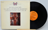A vinyl record album with its paper sleeve standing beside the black record on a stand. The sleeve is cream-colored with printed text and a Union Jack themed cover image, and the record has an orange center label.