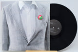 A vinyl record partially covering a printed sleeve or cover art showing a mannequin torso in a light gray plaid blazer over a white shirt with a small red and green pin at the chest. The black record is visible on the right against a light gray background.