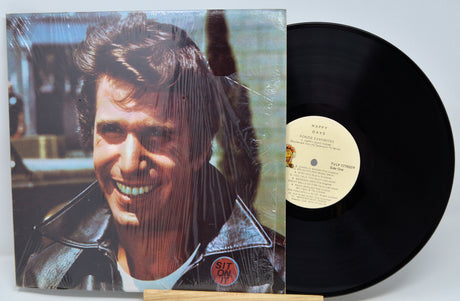 Vinyl record with cover featuring a smiling person, on a light gray background