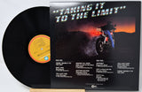 Vinyl record album 'Taking It to the Limit' with the black LP partially visible behind the printed sleeve, photographed on a white background.