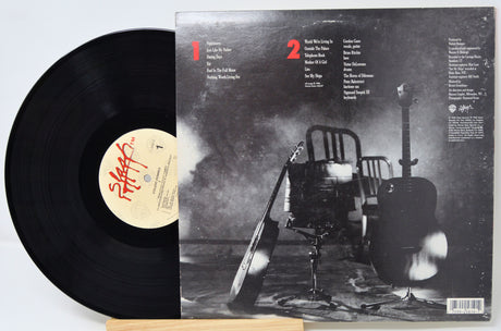 Vinyl record with cover featuring a black and white image of a chair and guitar.