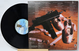 Vinyl record with a cover featuring a gun and shoes on a wooden floor.
