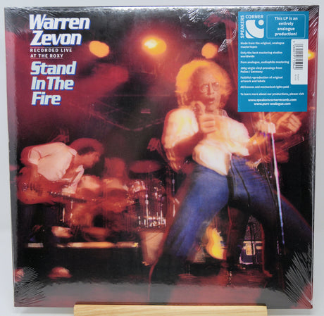 Warren Zevon 'Stand In The Fire' vinyl record LP cover, sealed in shrink wrap, displayed on a small wooden stand against a white background. The cover features a live concert photograph with a blue 'Corner Store' condition sticker in the top right.