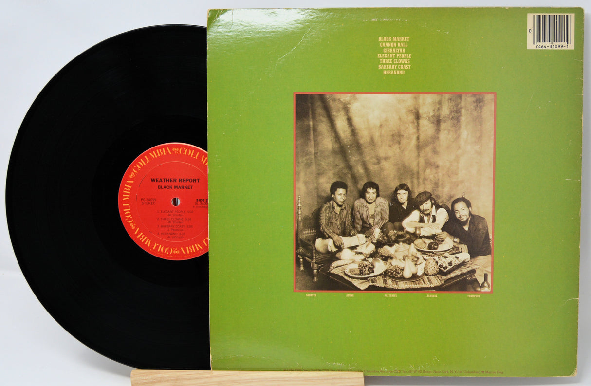 Vinyl record with green cover featuring a black and white photo of people around a table, on a white background.