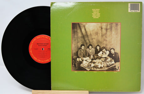 Vinyl record with green cover featuring a black and white photo of people around a table, on a white background.