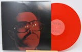 Vinyl record with a red disc and black cover featuring a face, on a white background.
