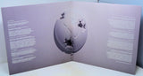 Open book with purple cover featuring a central circular design and text on either side.