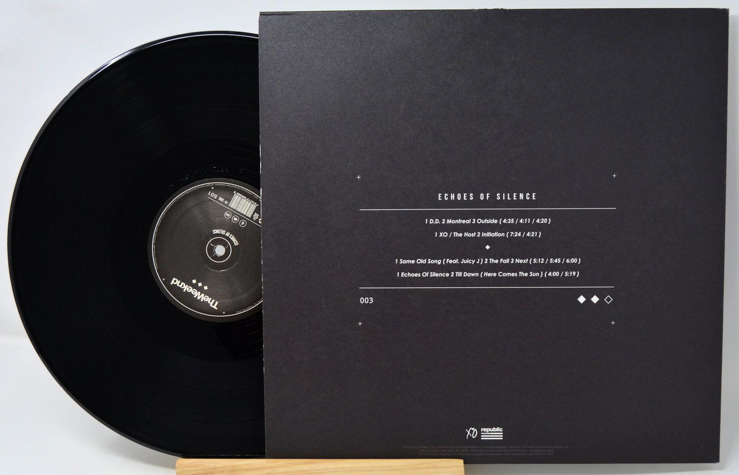 Black vinyl record with cover displaying tracklist on a white background
