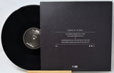 Black vinyl record with cover displaying tracklist on a white background