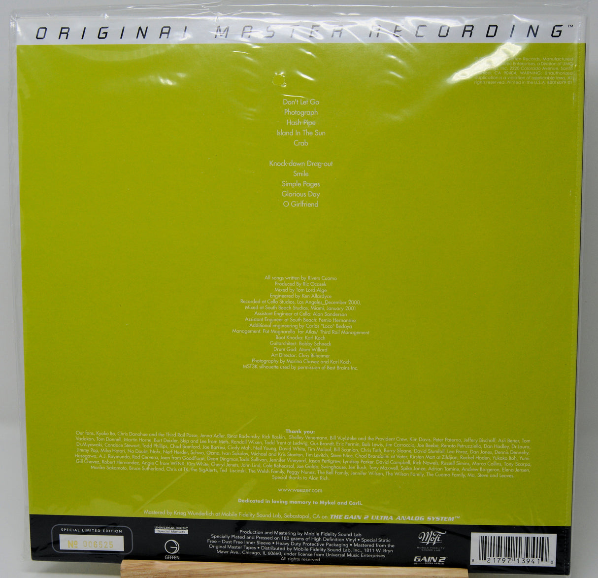The back cover of a vinyl record sleeve, featuring a bright lime green background with white text listing track titles and credits, sealed in its plastic shrink wrap.