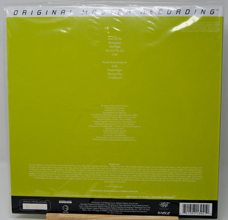 The back cover of a vinyl record sleeve, featuring a bright lime green background with white text listing track titles and credits, sealed in its plastic shrink wrap.