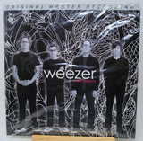 Weezer 'More Believe' original master recording vinyl LP with a shrink wrap sleeve, displayed on a wooden stand against a white background.