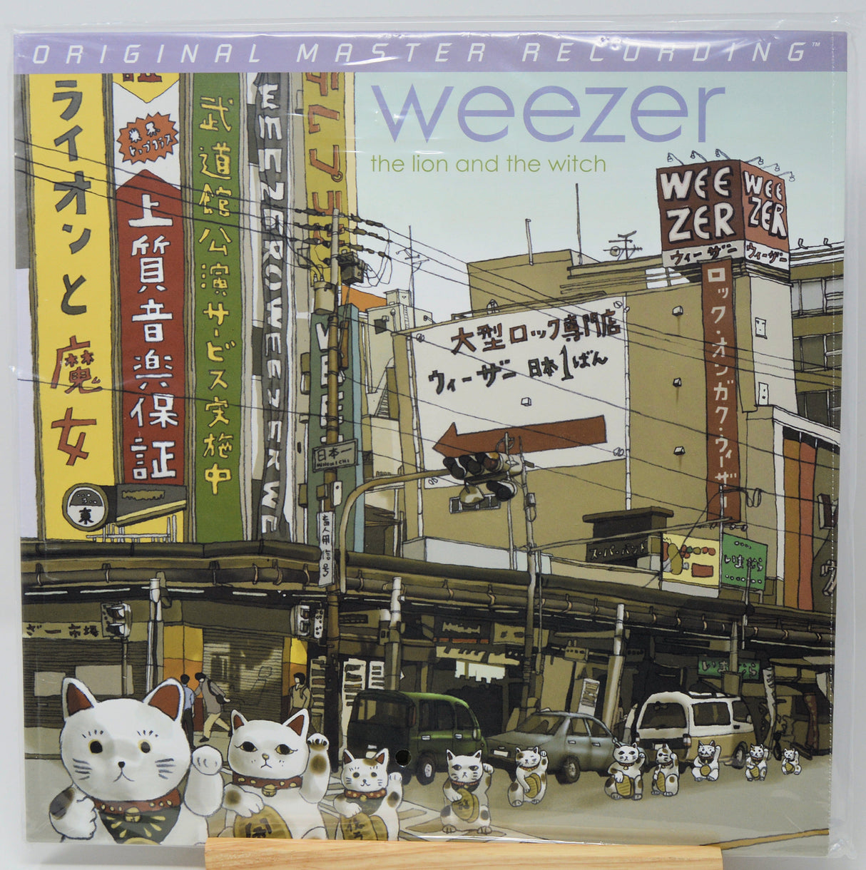 Weezer 'The Lion and the Witch' 12-inch vinyl LP cover, featuring an illustrated street scene with Japanese signs and multiple white mannequin cats in the foreground.