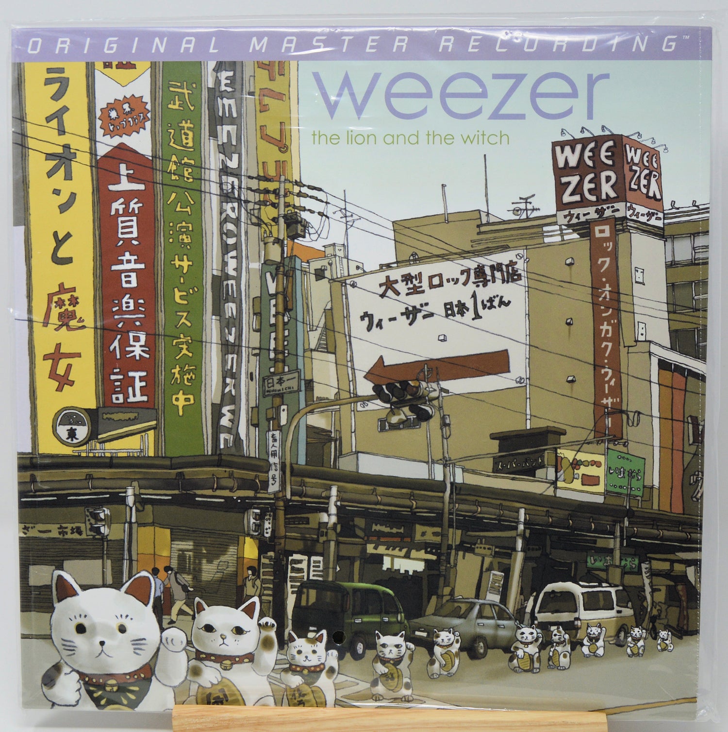 Weezer 'The Lion and the Witch' 12-inch vinyl LP cover, featuring an illustrated street scene with Japanese signs and multiple white mannequin cats in the foreground.