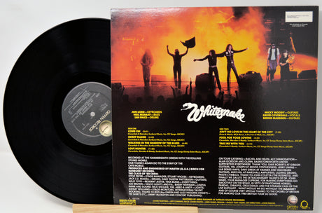 A vinyl record partially pulled from its back cover sleeve, showing the black record on the left and the printed back cover artwork on the right. The sleeve features a fiery orange-and-black concert scene with the Whiteknock logo and track listing text.
