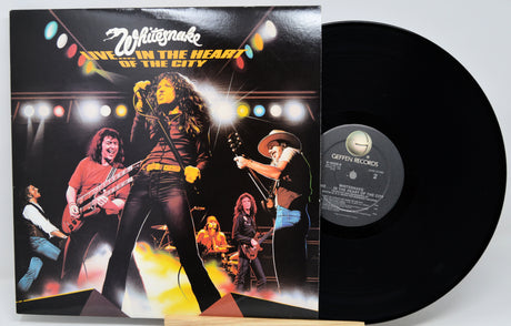 White Snake's 'Live in the Heart of the City' vinyl record LP with its illustrated cover sleeve and a black vinyl record partially visible, photographed against a light gray background.