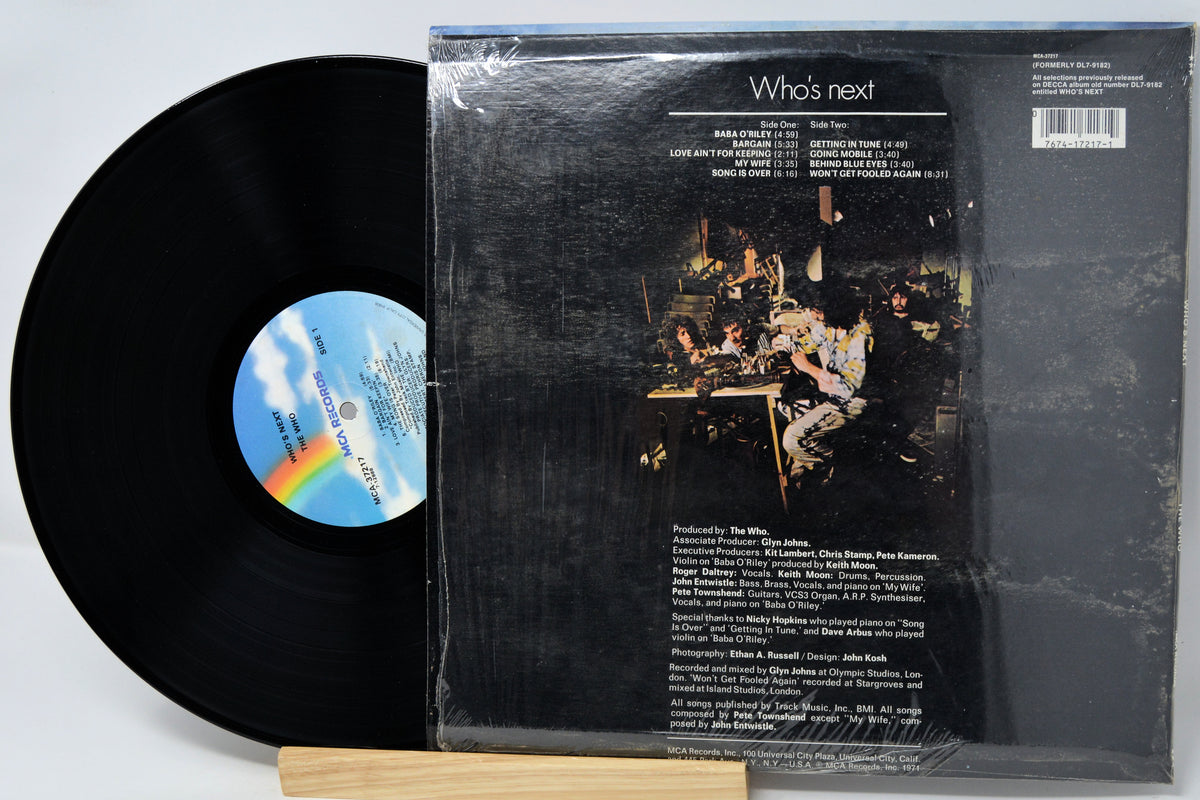 A vinyl record partially pulled from its sleeve, showing the black record and the back cover artwork for Who's Next. The sleeve is wrapped in clear plastic, with track listing text visible on the dark background.