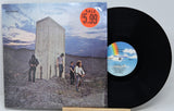 A vinyl record and its album cover for 'Who's next' by Axl Records, displayed on a small wooden stand against a light gray background. The cover features a desert landscape with a large concrete structure and three figures under a cloudy sky, with a red 'SALE $5.