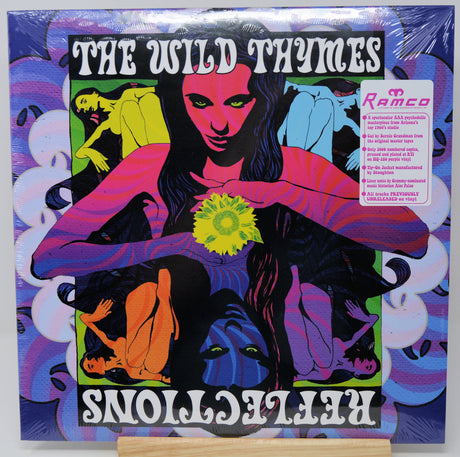 Vinyl record album cover for 'The Wild Thymes - Reflections' on a small wooden display stand. The cover features a psychedelic, high-contrast illustration with multiple stylized figures and faces in pink, purple, blue, green, orange, and black, wrapped in clear plastic.
