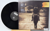A vinyl record partially pulled from its album jacket, showing the black record on the left and the back cover artwork on the right. The cover features a sepia-toned photo of a rider on a horse from behind, with track listing text and a small orange label area in the top right.