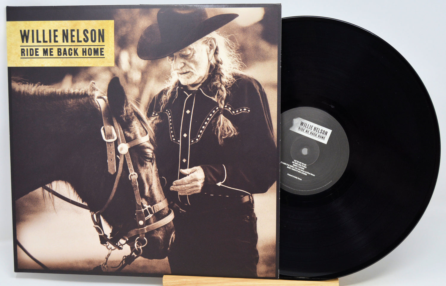 Willie Nelson 'Ride Me Back Home' vinyl record LP with the album cover and black record partially visible, displayed on a small wooden stand against a light gray background.