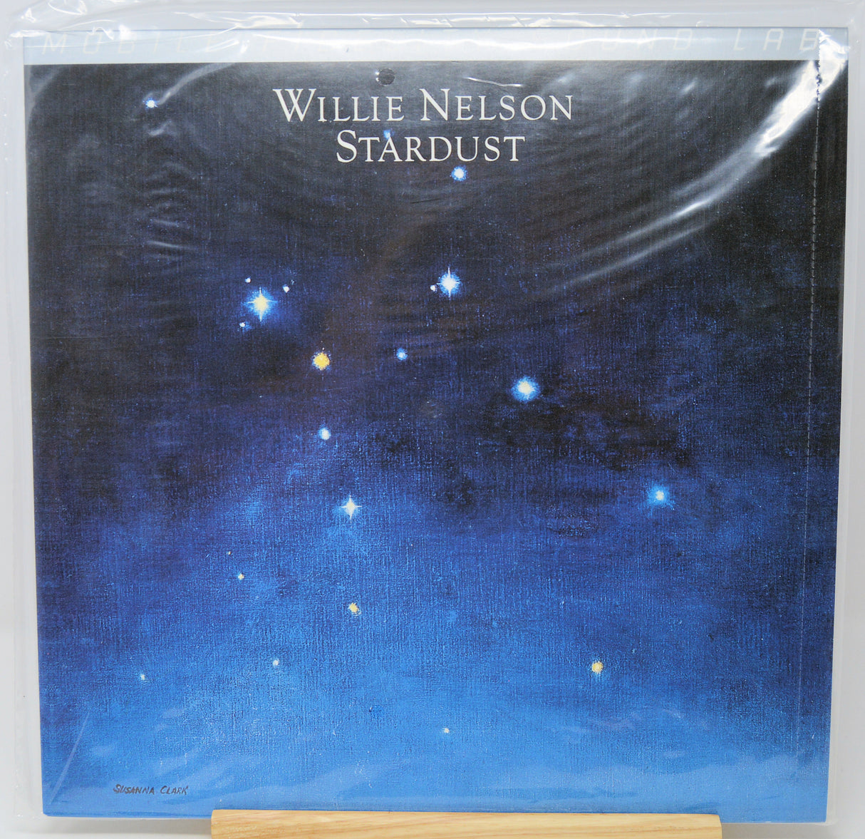 Willie Nelson 'Stardust' vinyl record cover, sealed in clear plastic shrink wrap and displayed on a wooden stand against a white background.