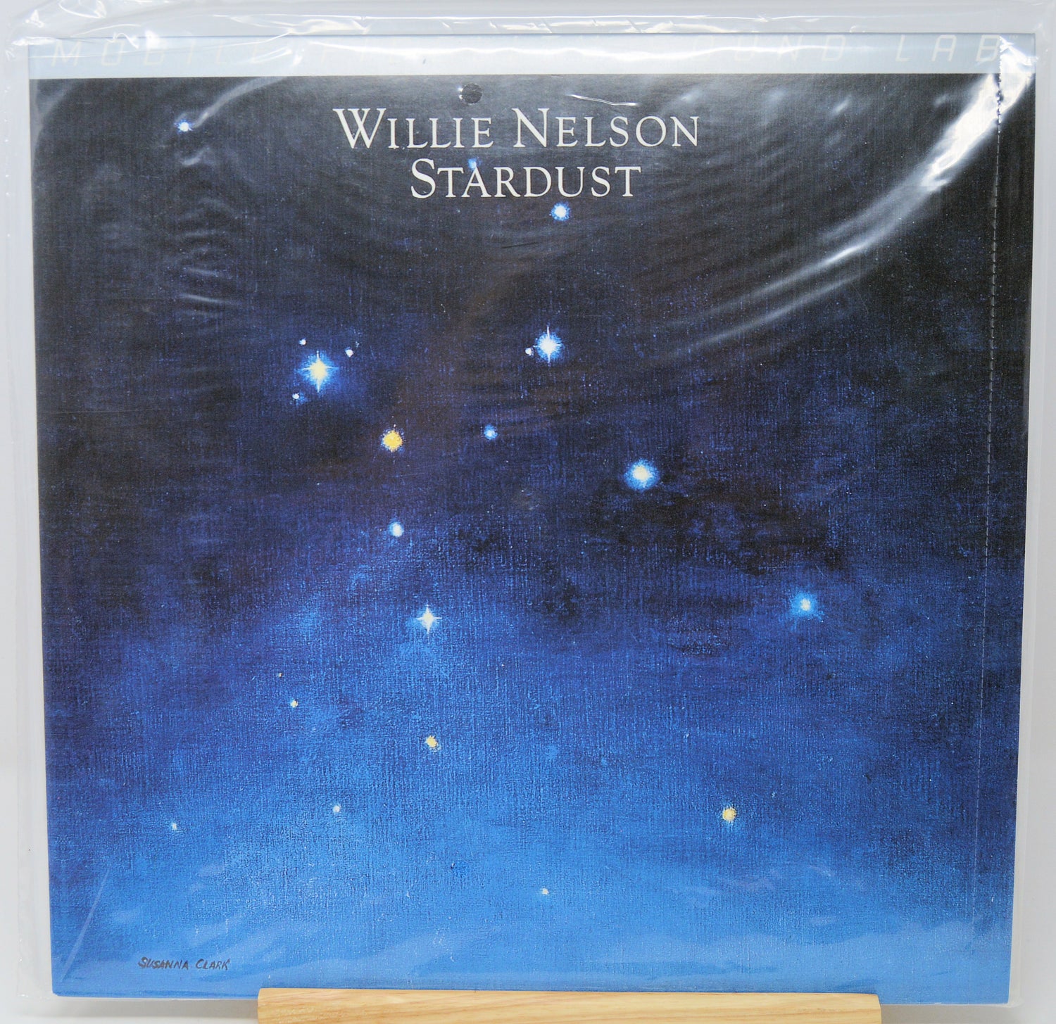 Willie Nelson 'Stardust' vinyl record cover, sealed in clear plastic shrink wrap and displayed on a wooden stand against a white background.