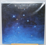 Willie Nelson 'Stardust' vinyl record cover, sealed in clear plastic shrink wrap and displayed on a wooden stand against a white background.