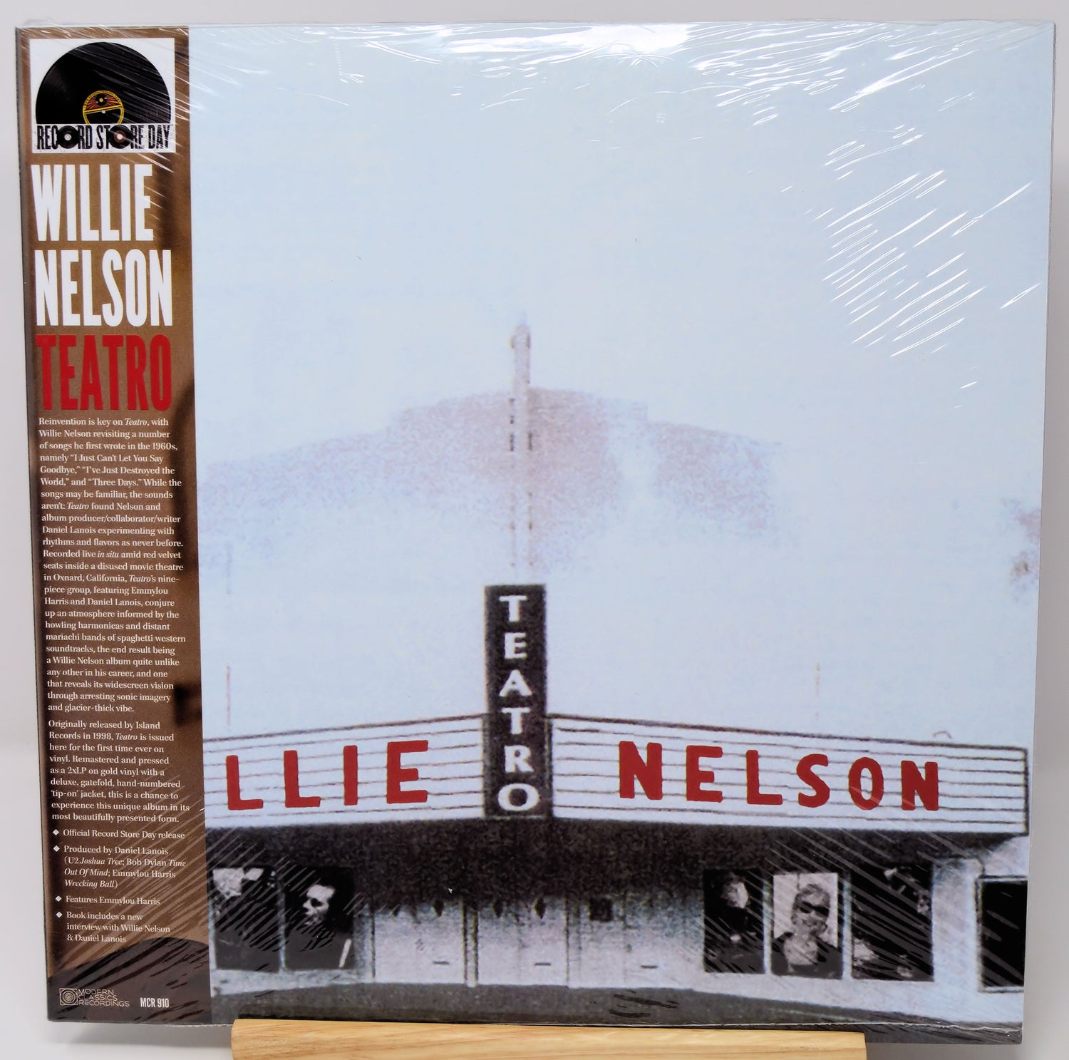 Willie Nelson 'Teatro' vinyl record LP on a wooden display stand, sealed in shrink wrap. The cover features a faded photograph of the Teatro Nelson building with bold red lettering, and the left sleeve displays the artist's name and tracklist.