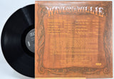 A vinyl record partially pulled from its printed sleeve, showing the back cover artwork. The black record has a visible RCA label, and the sleeve is tan and brown with ornate border graphics and the text 'Waylon & Willie' at the top.