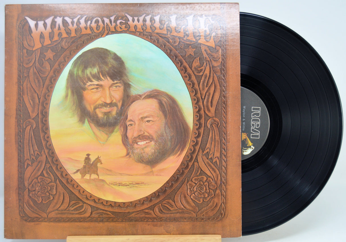 A vinyl record partially pulled from its album cover, showing the front artwork for Waylon & Willie's 'The Waylon & Willie Album' on a plain light background.