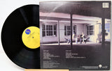 Vinyl record with a yellow label and cover featuring a black and white photo of a house.