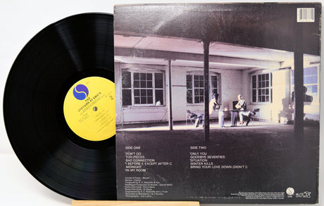 Vinyl record with a yellow label and cover featuring a black and white photo of a house.