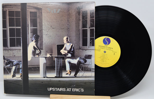 Vinyl record with cover showing a black and white photo of people in a room, featuring a yellow label.