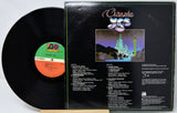 A vinyl record shown with its back cover open, displaying the tracklist and printed artwork. The black record is partially pulled from the sleeve, and the center label shows a green and orange PG Ratings logo.