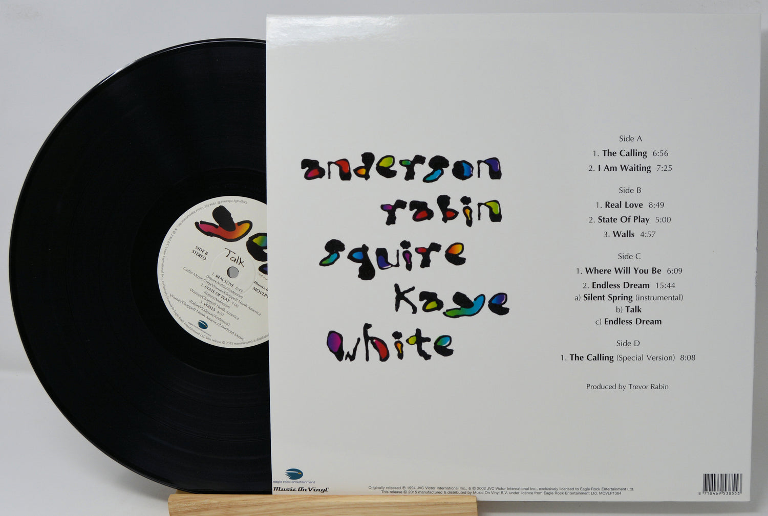 Vinyl record album shown with the black record partially visible on the left and the white outer sleeve on the right, displayed upright on a small wooden stand against a light gray background.