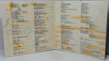 An open booklet or instruction manual spread open on a light gray surface, showing printed maps, technical diagrams, and dense text in blue and orange on an off-white background.