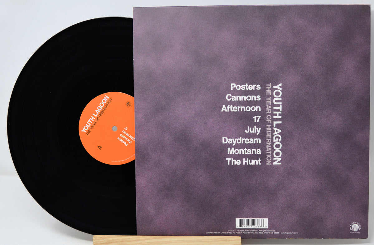 A vinyl record partially pulled from its sleeve, showing a black disc with an orange label next to a mauve-purple cover printed with tracklist text and the band name YOUTH LAGOON.