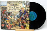 A vinyl record of Frank Zappa's album 'Grand Wazoo' with a colorful, artistic cover featuring a crowd and musical instruments.