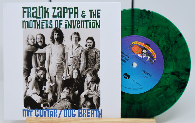 A green splatter vinyl record titled 'Frank Zappa & The Mothers of Invention - My Guitar / Dog Breath'. The cover shows a group photo of the band members.