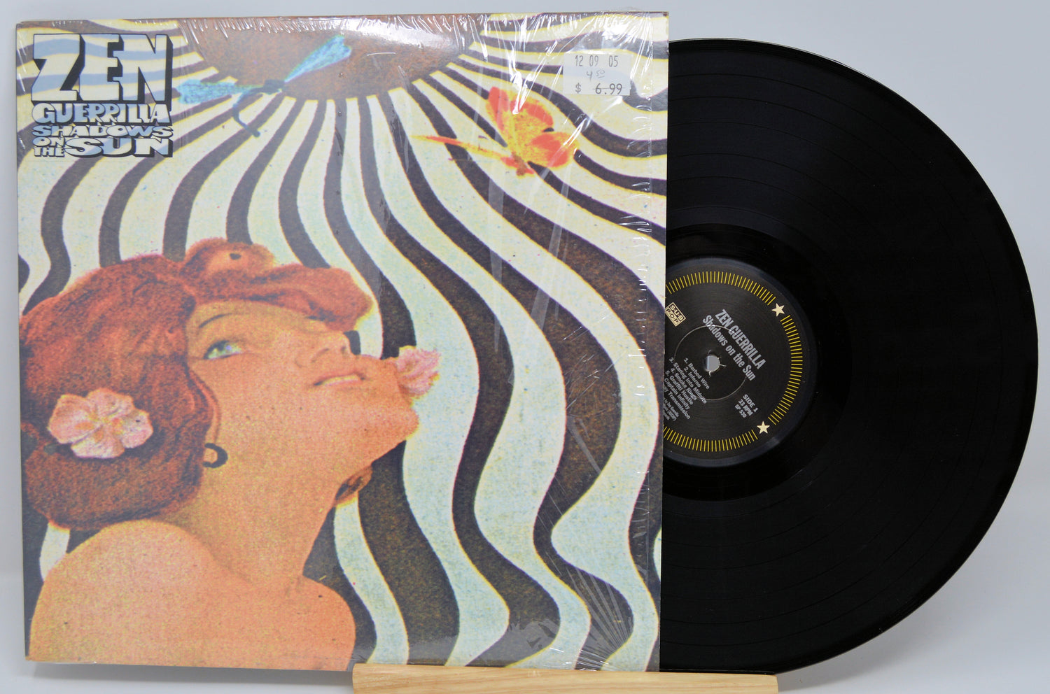 Vinyl record and cover for the album 'Zen Guerilla - Shadows On The Sun' with a striped background and a woman's face in the center.