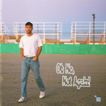 The image shows the cover art for the Alexander 23 album 'Oh No Not Again.' It features a man in a white t-shirt and blue jeans, standing with his hands in his pockets, against a faded green backdrop.