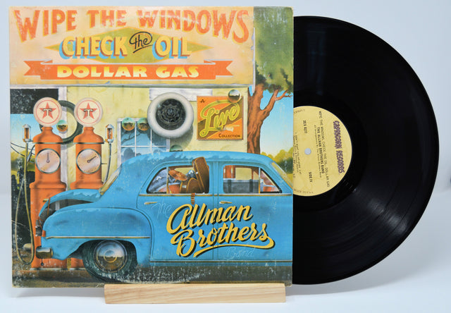 Vinyl record with a colorful cover featuring an illustration of a blue car and vintage gas station, with text 'Wipe the Windows, Check the Oil, Dollar Gas'.