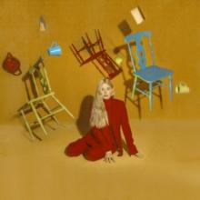 A vinyl record cover featuring a woman sitting cross-legged on a floor with various abstract-designed chairs and a handbag in the background, against a beige background.