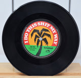 A 7-inch record with a label featuring text and a palm tree graphic. The record is black, with a red and yellow label.